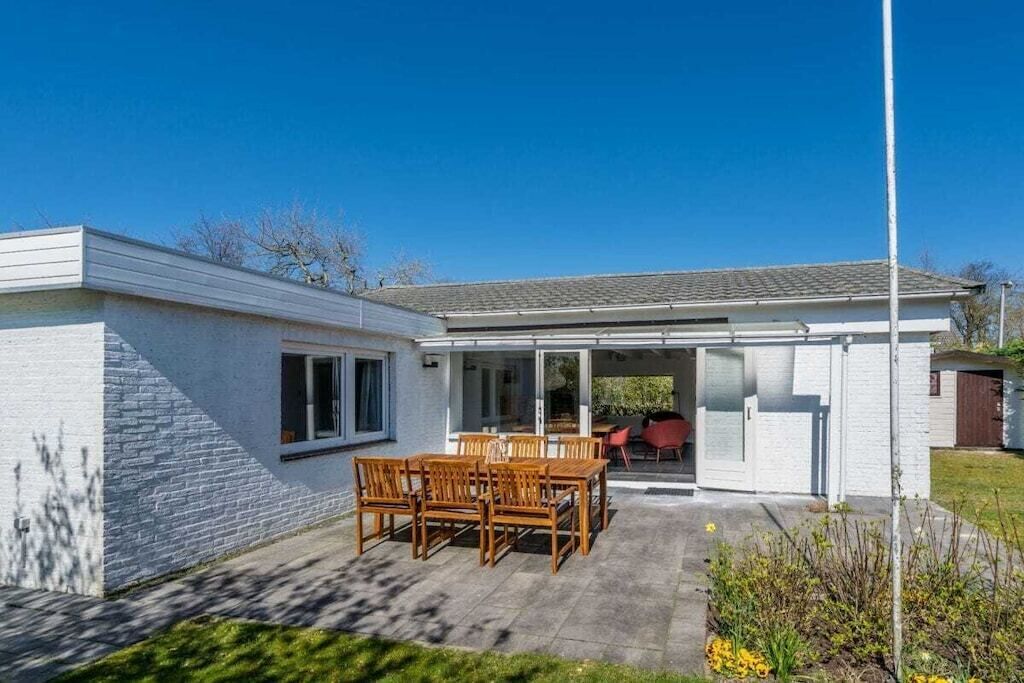 A modern house with a patio, a dining area with wooden furniture, and a covered outdoor space.