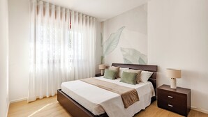 Un dormitorio con una cama, mesitas de noche, una lámpara y una pared con diseño de hojas.