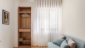 Una habitación con un armario de madera, un sofá azul y una ventana con cortinas translúcidas.