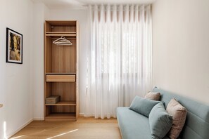 Una stanza con un'armadio in legno, un divano blu e una finestra con tende leggere.