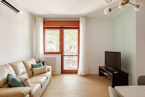 A living room with a sofa, a television, and a window with curtains.