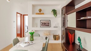 Un comedor moderno con una mesa blanca, sillas verdes y una estantería con diversos objetos.