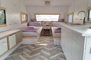 Ein kompaktes Wohnmobil-Interieur mit zwei Schlafbereichen, einer Küchenzeile und einem Fenster für natürliches Licht.