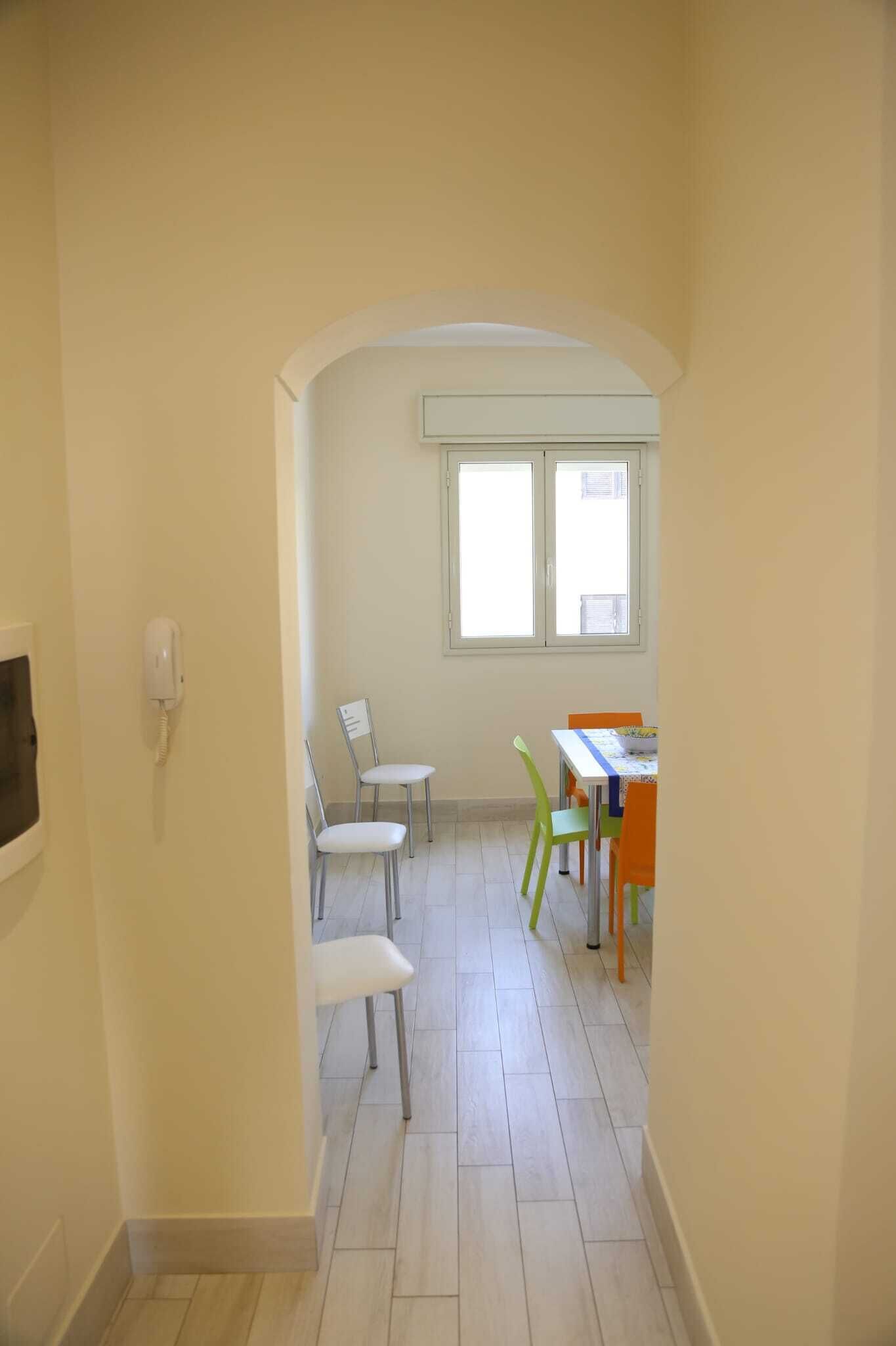 Un couloir avec une porte donnant sur une pièce qui contient une fenêtre, un téléphone et plusieurs chaises.