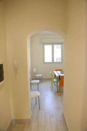 Un couloir avec une porte donnant sur une pièce qui contient une fenêtre, un téléphone et plusieurs chaises.