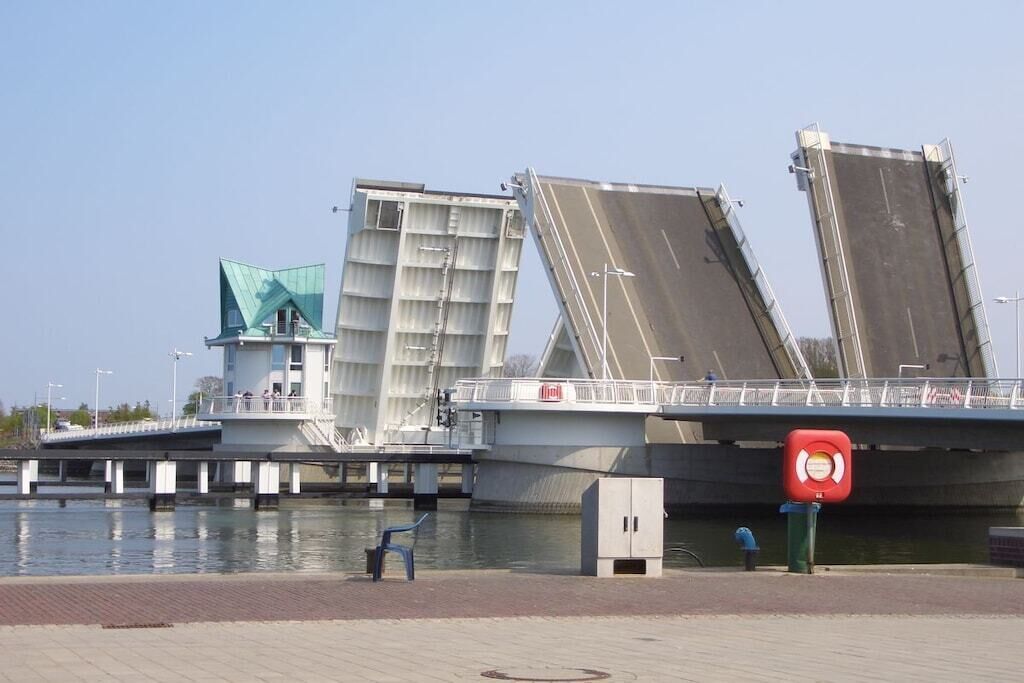 A bridge with large, open gates over water, a small building with a green roof, and a red sign with a white symbol.