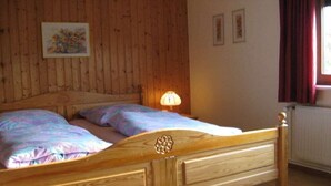 Cama de madeira com cabeceira, duas almofadas e um abajur em um quarto com paredes de madeira e uma janela com cortinas.