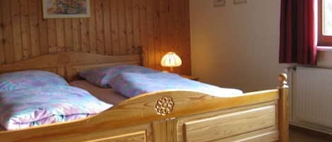 Ein hölzernes Bett mit Kopfteil, zwei Kissen und einer Nachttischlampe in einem Zimmer mit Holzwänden und einem fenster mit Vorhängen.