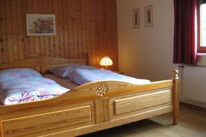 Un letto di legno con testiera, due cuscini e una lampada da comodino in una stanza con pareti in legno e una finestra con tende.