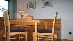 Uma área de refeições com mesa e cadeiras de madeira, uma tigela de laranjas e duas molduras na parede.