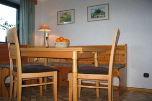 Zona pranzo con tavolo e sedie in legno, una ciotola di arance e due quadri appesi al muro.
