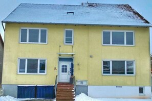 Ein zweistöckiges Gebäude mit einer gelben Fassade, einer weißen Tür und einer Treppe zum Eingang.