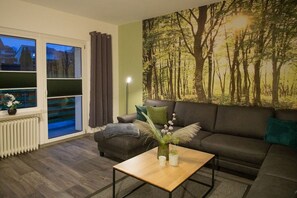 Een woonkamer met een bank, een salontafel, een raam met zonwering en een wanddecoratie.