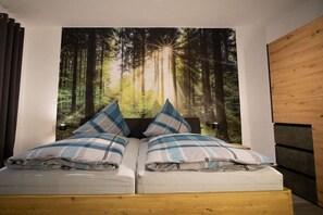 Een slaapkamer met een bed, een groot wandtapijt met een bosmotief en een houten hoofdeinde.