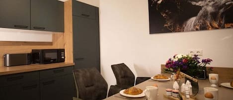 A modern kitchen with dark cabinets, a microwave, and a dining table set for breakfast with plates, cups, and a decorative centerpiece.