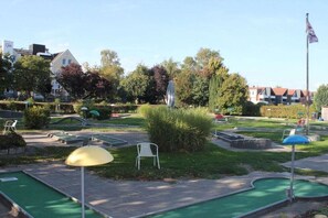 Ein Minigolfplatz mit grünen Spielbahnen, einer Fahnenstange und umgebender Bepflanzung.