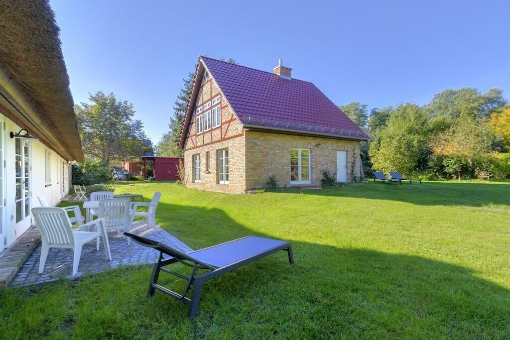 A house with a red-tiled roof, a thatched roof adjacent to it, and a lawn with outdoor furniture.