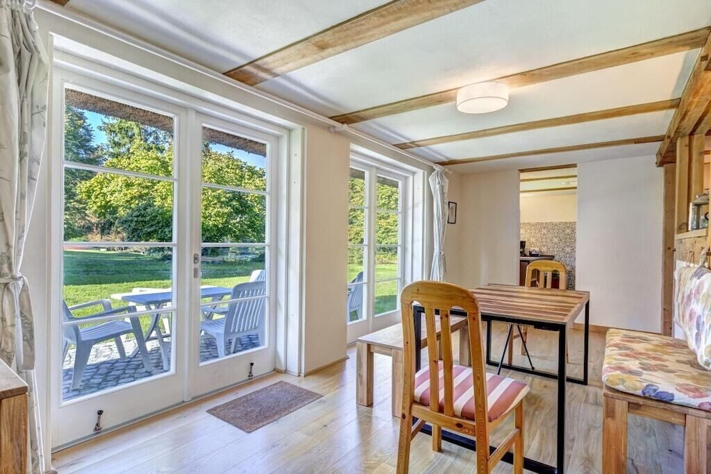 Een kamer met een houten plafond, een eettafel met stoelen, een bankje en uitzicht op een terras met stoelen en een tafel.