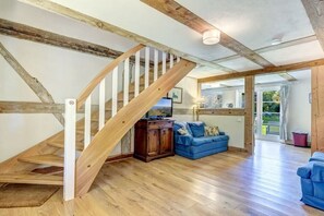 A wooden staircase leading to an upper level, a blue sofa, and a television in a living area with a view of the outdoors.