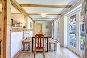 A dining area with wooden furniture, a ceiling with exposed beams, and a view through glass doors to the outside.