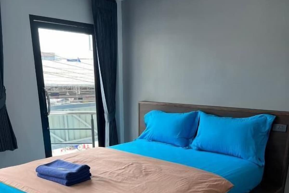 A modern hotel room with a large bed, a view through a window, and a balcony.