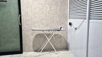 Una habitación con piso de baldosas, una tabla de planchar metálica y un enchufe eléctrico en la pared.