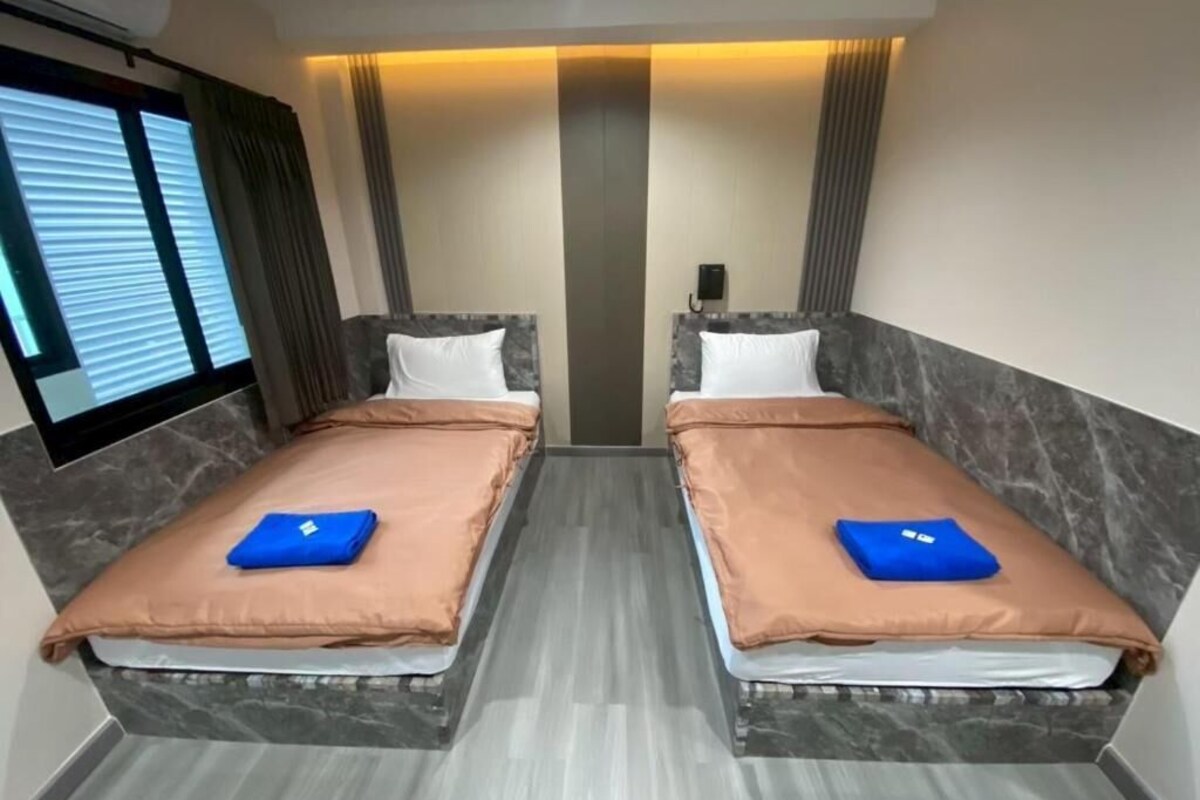 A hotel room with two beds, a flat-screen TV, and a window with blinds.