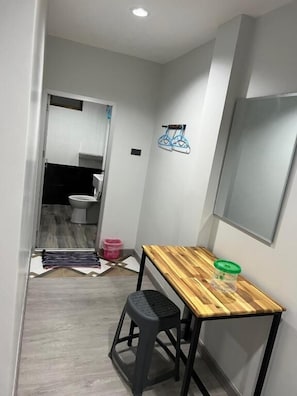 A small bathroom with a toilet, a mirror, and a wooden table with a stool. - CK Residence Hat Yai (Chang Wat Songkhla)
