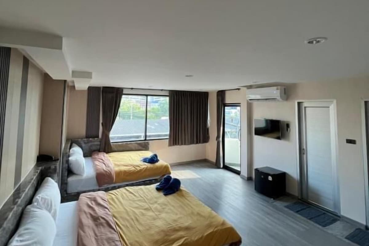 A hotel room with two beds, a large window, a door, and a small desk.