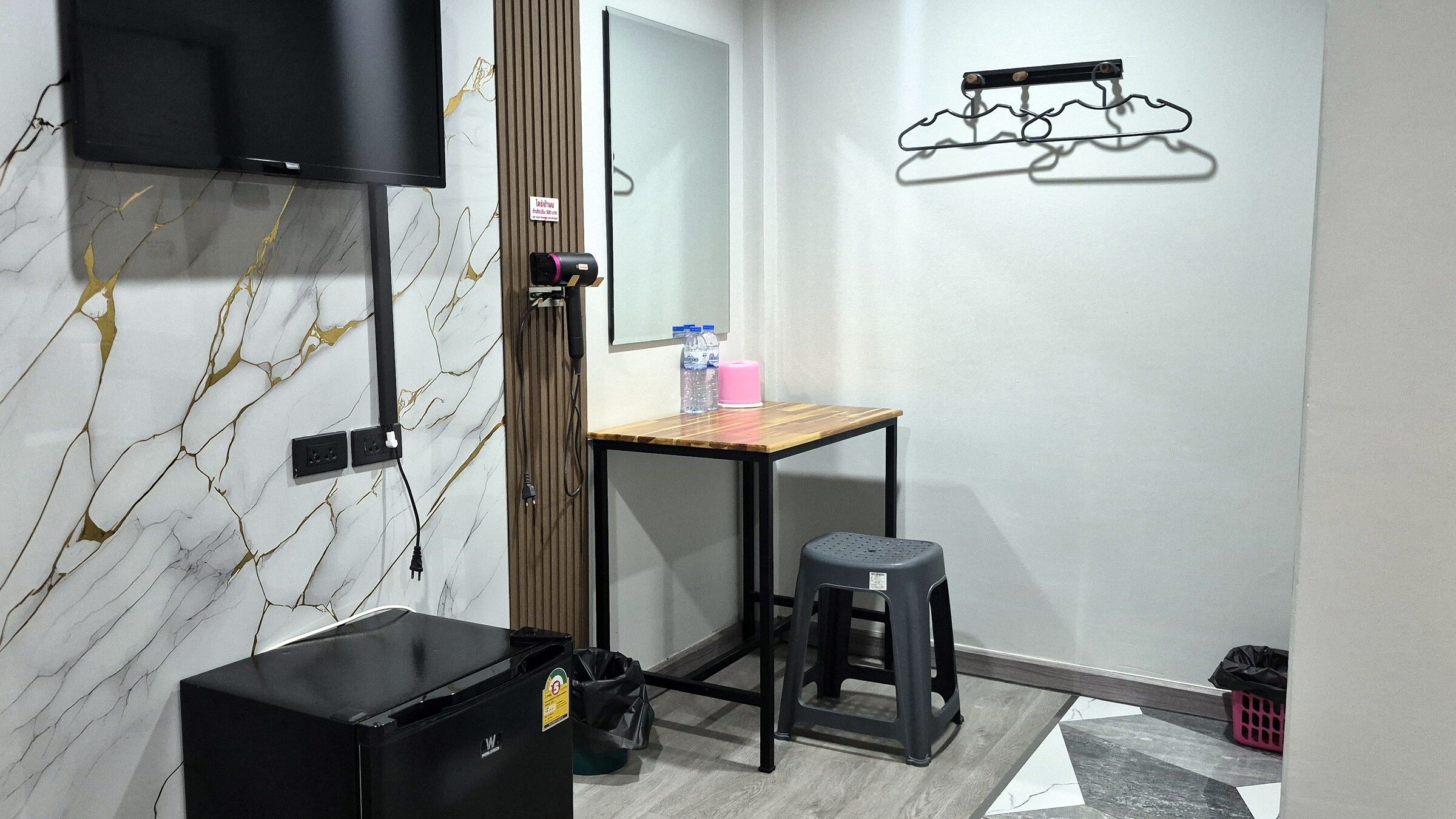 Una habitación pequeña y moderna con televisión, un escritorio de madera, un taburete y un mueble de almacenamiento negro.