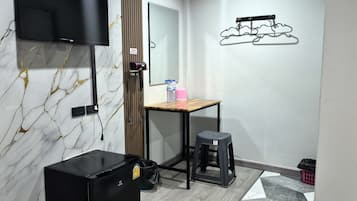 Una habitación pequeña y moderna con televisión, un escritorio de madera, un taburete y un mueble de almacenamiento negro.