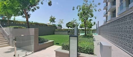 Área externa moderna com portão de vidro, placa de sinalização e jardim ajardinado.