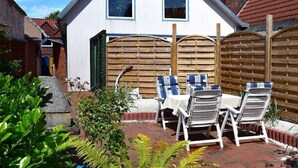A residential property with a patio area featuring a table and chairs, a wooden fence, and a brick wall. - Holiday apartment with 1 bedroom (Tönning)