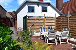 Una propiedad residencial con un patio que incluye una mesa y sillas, una cerca de madera y un muro de ladrillo.