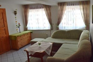 Una sala de estar con un sofá, un aparador de madera, una mesita con un vaso y una ventana con cortinas.