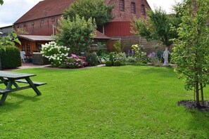 Ein gepflegter Garten mit Picknicktisch, einem Backsteinhaus und verschiedenen Pflanzen und Blumen.