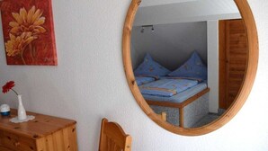 A bedroom with a bed, a wooden dresser, a mirror, and a painting on the wall. - Holiday apartment with 1 bedroom (Tönning)