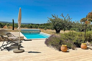 Ein Poolbereich mit Holzterrasse, Liegestühlen und einer Pergola.