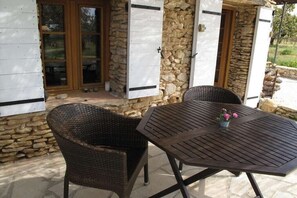 Ein Sitzbereich im Freien mit Korbstühlen und einem Tisch, Steinmauern und Holzläden.