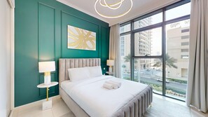 Une chambre moderne avec un grand lit, deux tables de chevet, une vue sur la ville grâce à de grandes fenêtres et un mur d’accent de couleur verte.