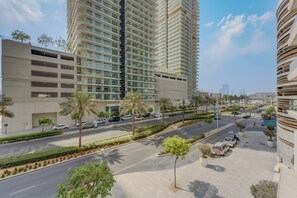 A modern urban street with high-rise buildings, palm trees, and a clear sky. - Luxe 1 Bed l Private Beach Access & City Views (Emaar Beachfront)