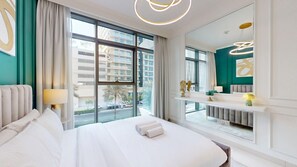 A hotel room with a large bed, a view of the city, a vanity with a mirror, and a modern light fixture. - Luxe 1 Bed l Private Beach Access & City Views (Emaar Beachfront)