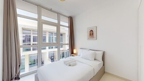 A hotel room with a large window, a bed with white linens, a bedside table with a lamp, and a framed picture on the wall.