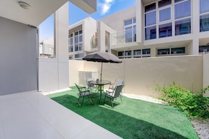 A courtyard with artificial grass, a table with chairs, and a black umbrella. - Private 3 Bed Villa with Garden l Malibu Waterpark (DAMAC Hills 2)