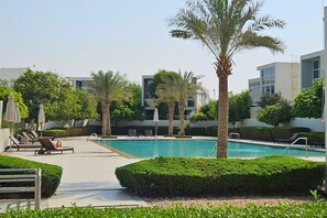 A swimming pool with lounge chairs and palm trees, surrounded by modern buildings.
