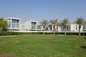 A modern building with a flat roof, large windows, and a grassy courtyard with palm trees.