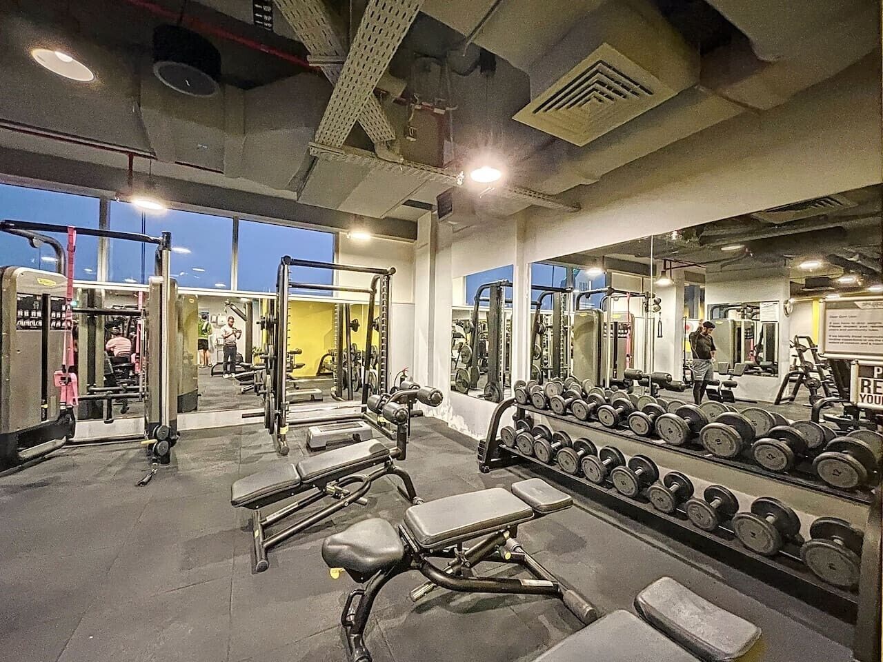 A gym with weightlifting equipment, benches, and a mirror reflecting the space.