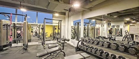 Ein Fitnessraum mit Krafttrainingsgeräten, Bänken und einem Spiegel, der den Raum wiedergibt.