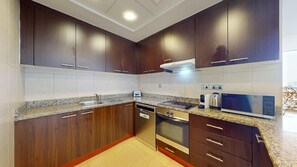 A modern kitchen with dark wood cabinets, granite countertops, stainless steel appliances, and a built-in microwave. - Bustling 2 Bed in DIFC l near Museum of the Future (DIFC)