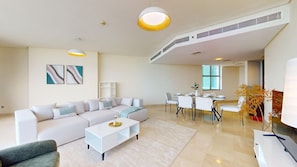 A modern living room with a sectional sofa, a coffee table, and a dining area with a table and chairs. - Bustling 2 Bed in DIFC l near Museum of the Future (DIFC)
